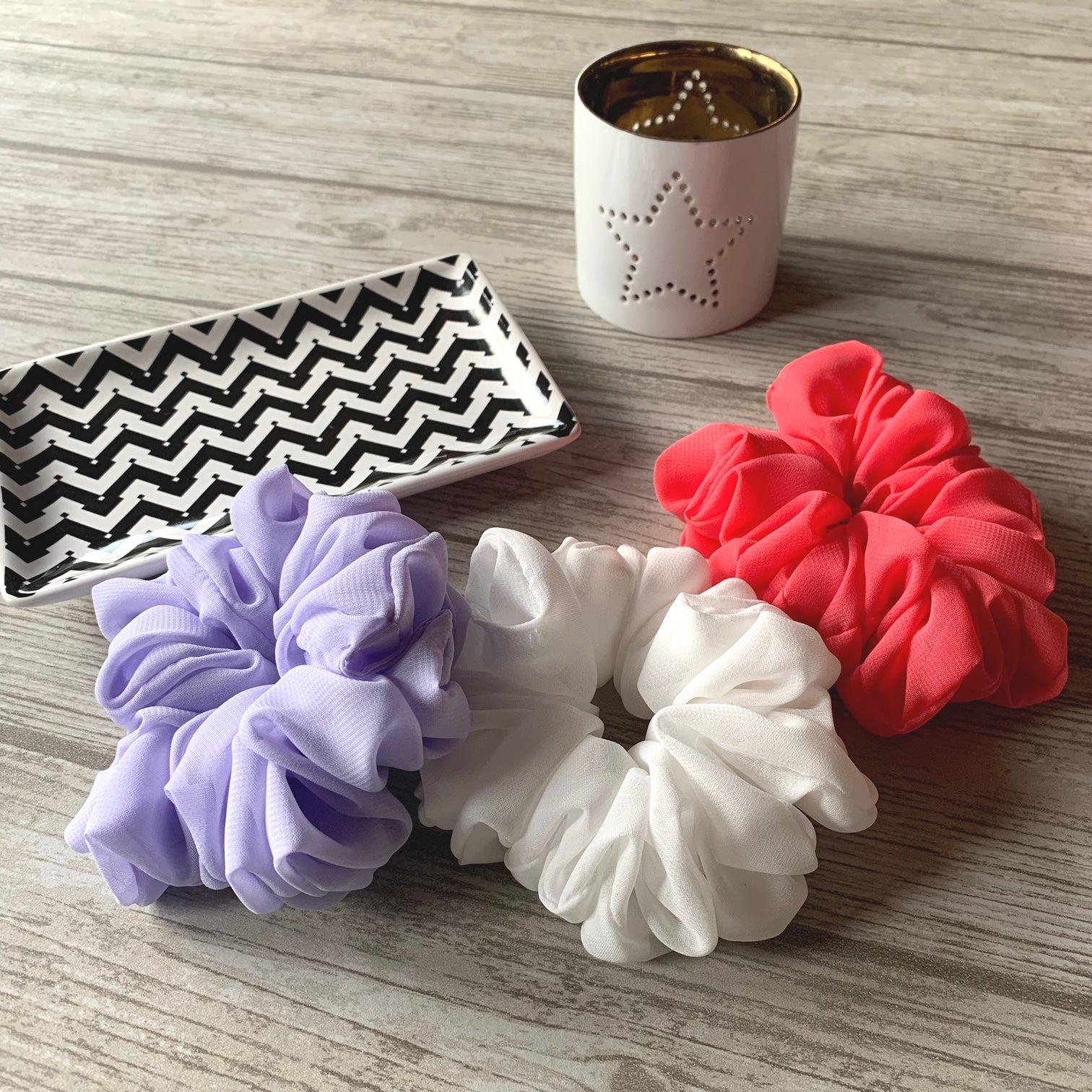 Lavendel, korall, vit scrunchie på bordet med en vit ljushållare med en stjärna på samt ett fat med svart/vit zigzag mönster
